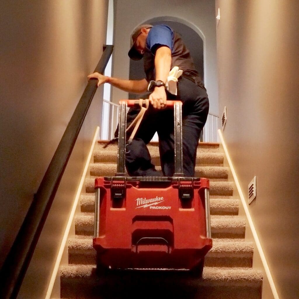 Man carrying toolbox up a carpeted staircase.
