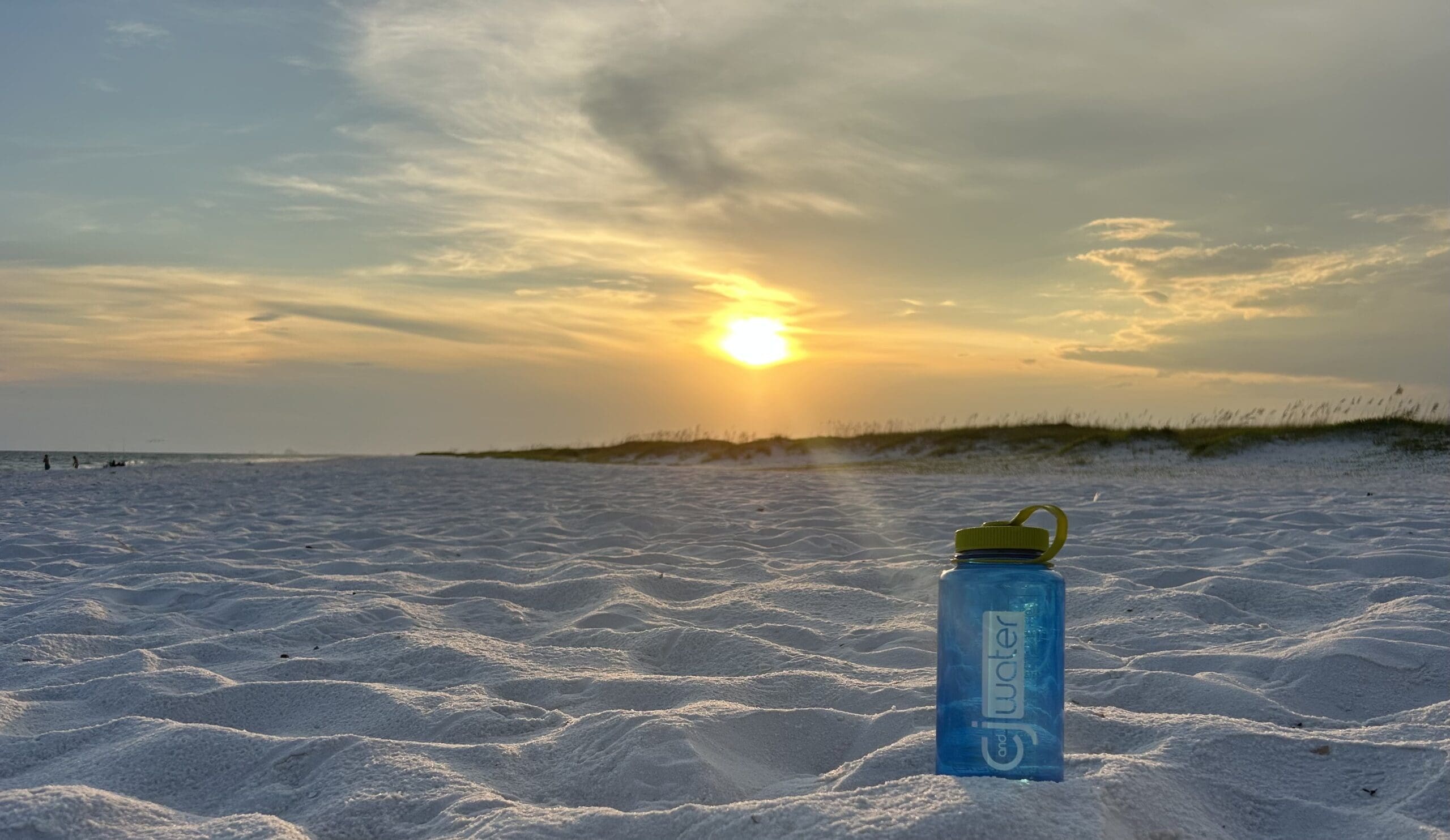 Water bottle labeled C&J on sandy beach.