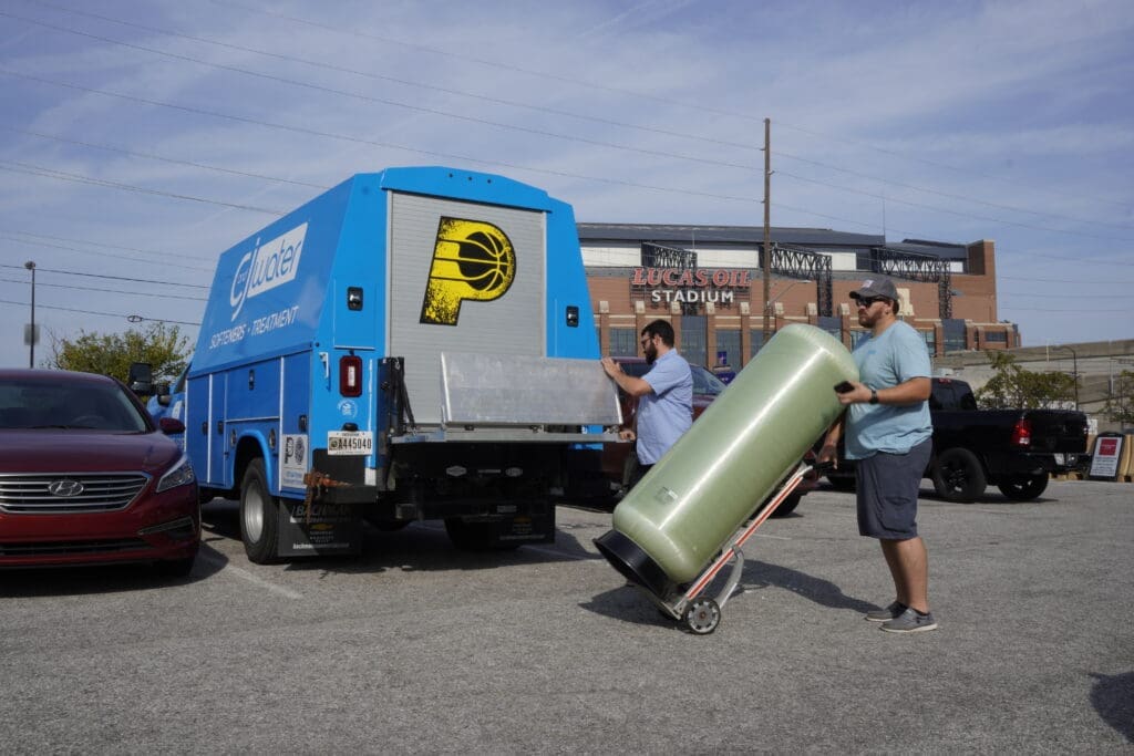 Workers unloading tank from blue C&J truck.