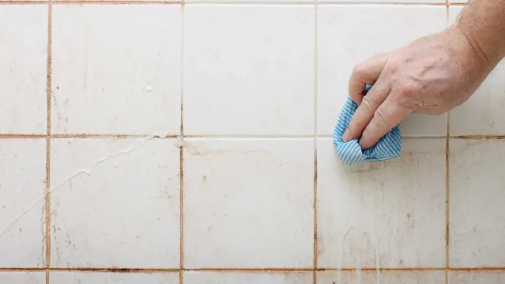 Hand wiping dirty white tiles with blue cloth.