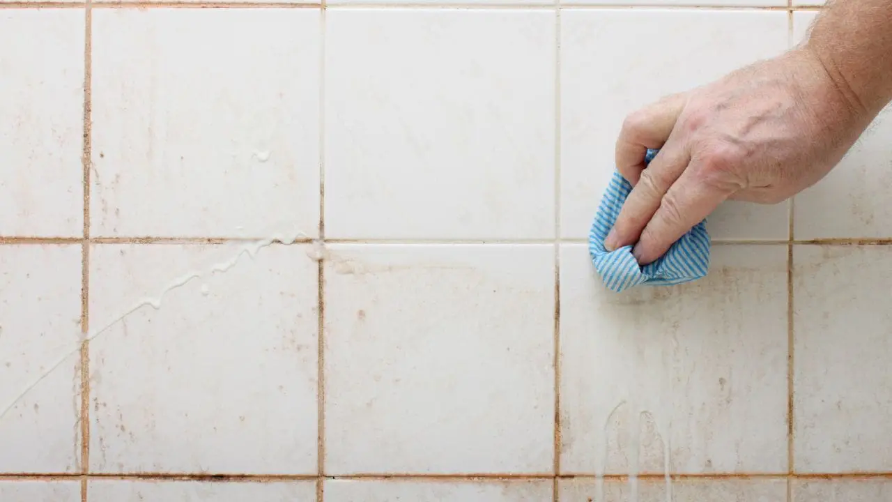 Hand wiping dirty white tiles with blue cloth.