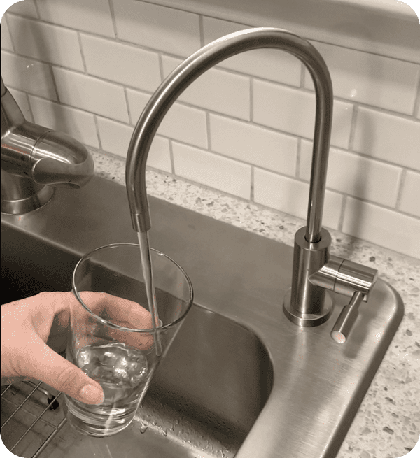 Hand filling glass under kitchen faucet.