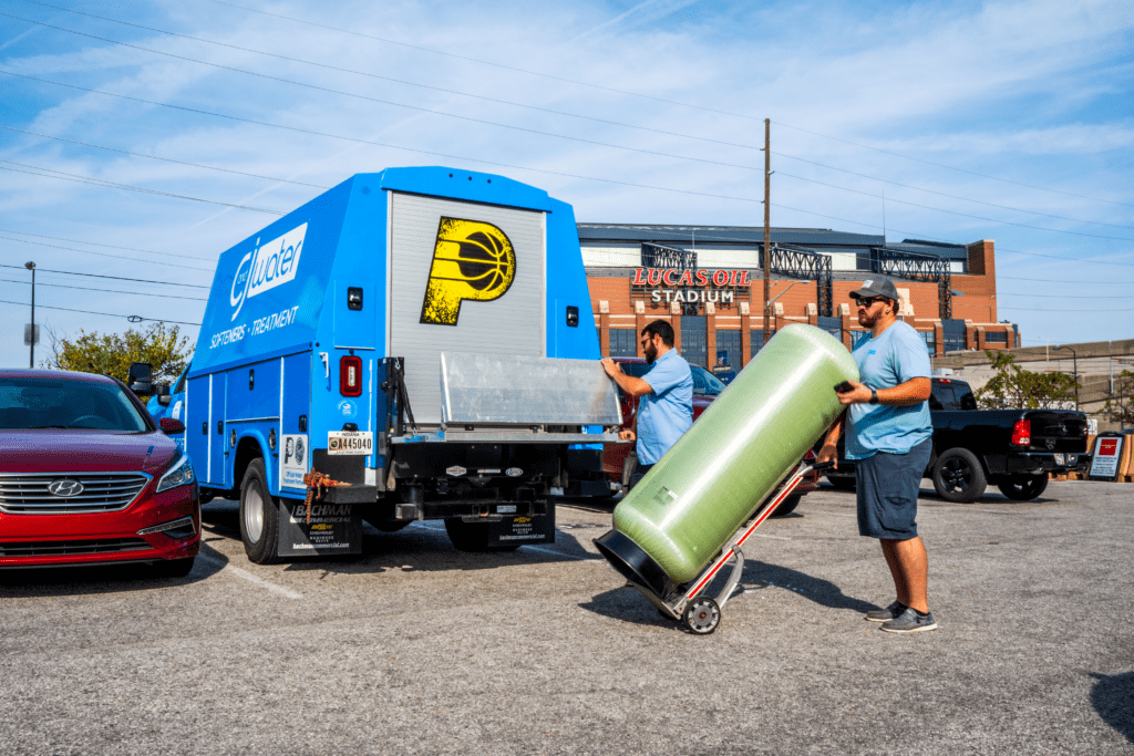 Water treatment technician moving a large fiberglass filtration tank from a service truck for installation