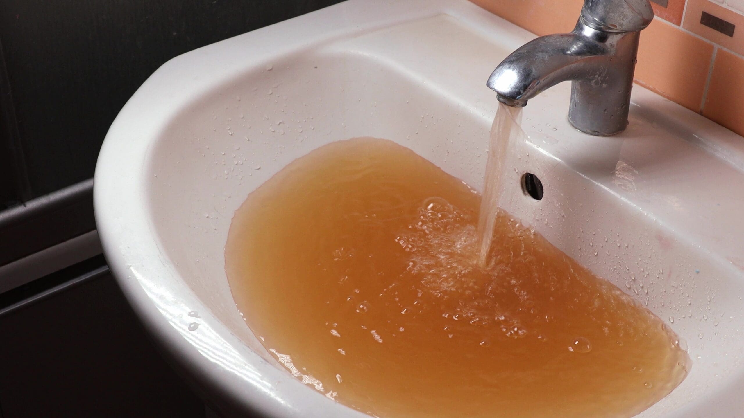 Brown rusty water flowing from a bathroom faucet into a white sink.