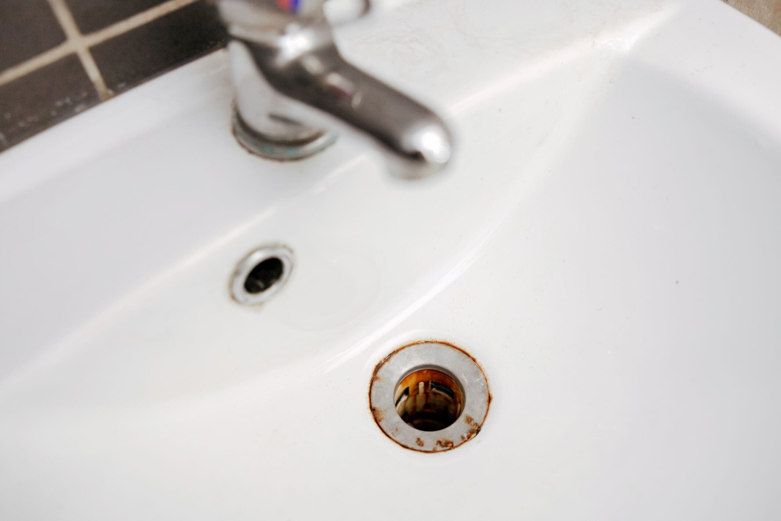 Rust-colored staining around a bathroom sink drain caused by iron in water.