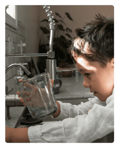 Child filling a glass at a kitchen sink.